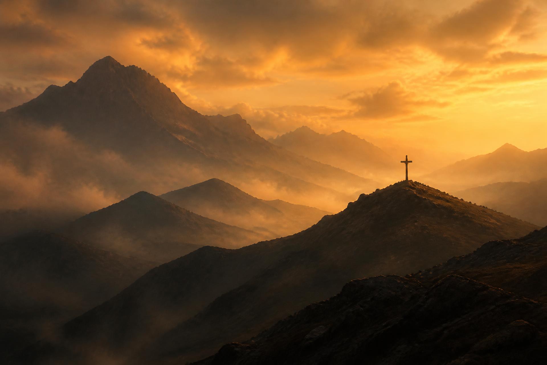 Misty mountain ridges at dawn with a small cross silhouetted on a distant summit